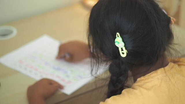 Young student girl writing on worksheet, doing homework at desk, learning.