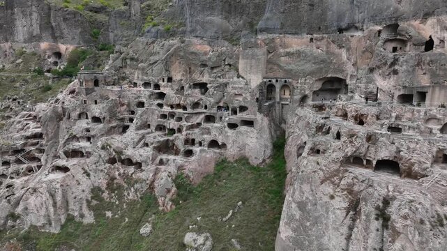 Vardzia cave monastery aerial view revealing the ancient rock hewn city and historical landmark with tourists exploring the archeological site in southern Georgia