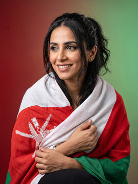 beautiful arab woman with dark hair holding oman flag with emblem on red and green background