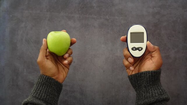 Person holding apple and glucometer for diabetes check representing healthy food choice.