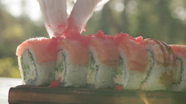 Gloved hand of a sushi chef decorates fresh rolls with tiny red roe creating an appetizing seafood topping during the detailed process of Japanese cuisine preparation