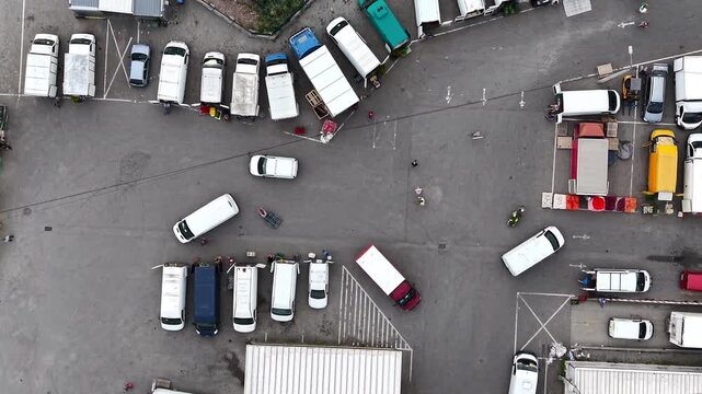 Aerial view of busy farmers market with trucks and vans parked along street. Vibrant produce and bustling activity among vendors and customers. Lively atmosphere of shoppers engaging for fresh produce