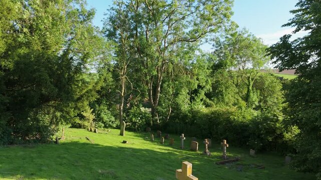 Sunlit green graveyard with trees and stone markers. Chapel