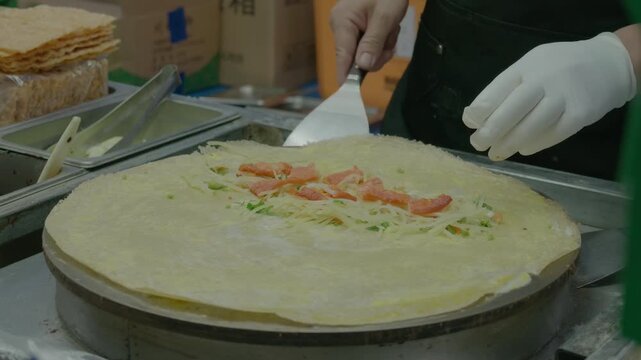 A chef prepares flatbread topped with seafood and vegetables on a cooking surface in a kitchen.