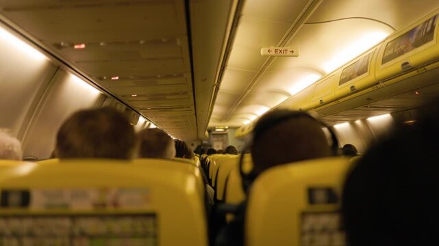 Passengers sit in rows of seats inside a commercial airplane cabin during flight with warm interior lighting creating a calm and comfortable travel atmosphere