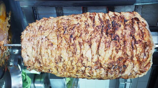 Large juicy chicken doner kebab shawarma spinning on vertical spit rotisserie grill cooker.