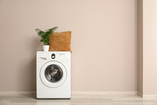 Home interior design and laundry room organization, modern washing machine with decorative pillow and houseplant against a beige wall background