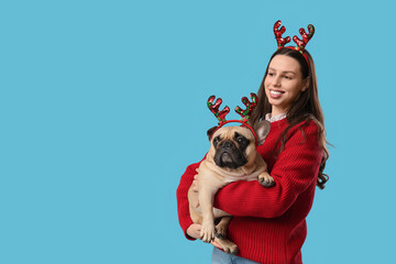 Christmas holiday celebration, happy woman with french bulldog wearing reindeer antlers headband for festive winter season party on blue background © Pixel-Shot