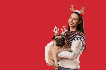 Christmas holiday joy, happy woman with cute french bulldog wearing reindeer antlers for festive winter celebration on a solid red background © Pixel-Shot