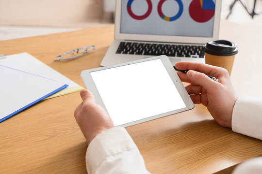 Digital transformation and business analytics, person using tablet with blank screen for mockup at office desk with laptop and financial charts