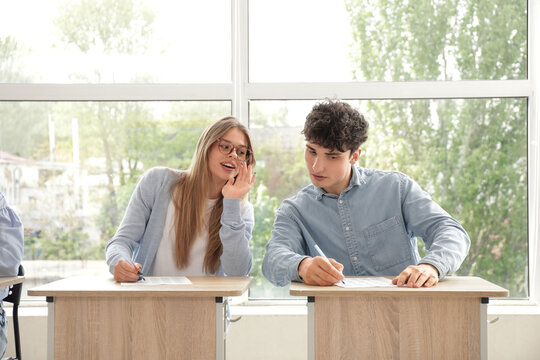 Academic dishonesty and cheating, student whispering answers to classmate during exam in school classroom with focus on education and integrity