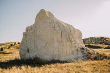 pale chalk outcrop rises from dry grassy slope under warm late afternoon sun, showing erosion geology in arid © Vulp