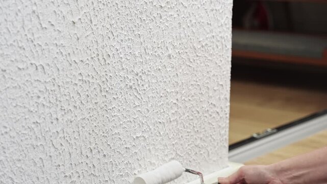 Painting textured apartment wall with a small white roller during restoration work