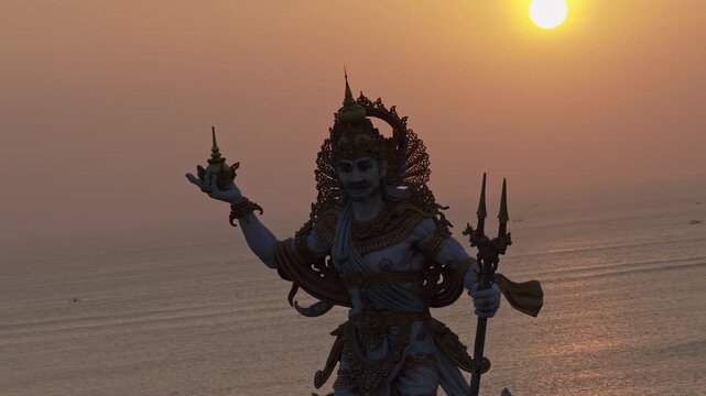 Sunset sky glowing over Bali ocean horizon illuminating giant Dewa Baruna statue at Kuta Beach iconic Indonesian tourist attraction travel destination aerial drone footage
