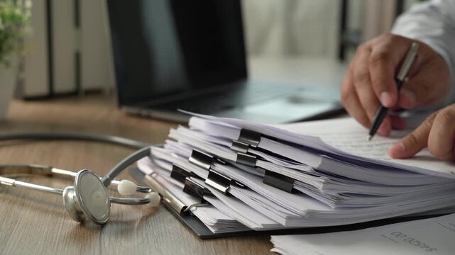 Hands sorting and turning stacked clipped documents on a desk, showing document management, file review and office administration workflow.