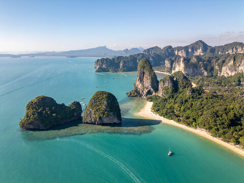 Aerial view of white sand Phra Nang Beach, two forested rock islets and tall limestone cliffs above clear turquoise water at Railay in Krabi, Thailand