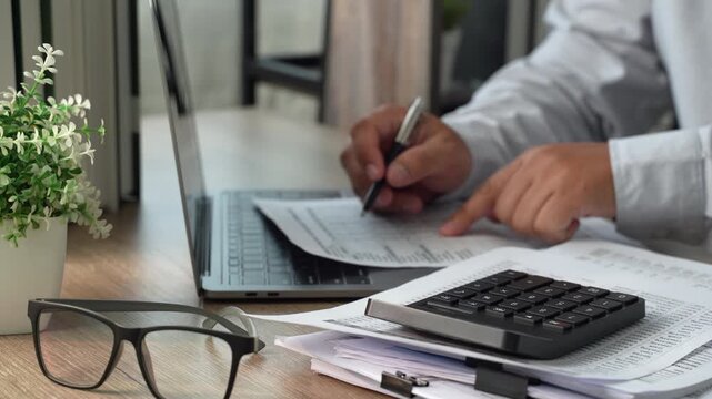 Hands reviewing stacked healthcare paperwork beside stethoscope and laptop, showing medical document review, records checking and clinical administration workflow.