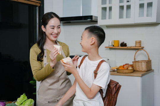 Smiling Asian family enjoying breakfast in weekend morning. Mother And son, cooking, and sharing joyful at the dining table in the kitchen together.