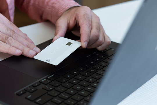 A person holds a bank credit card over a laptop and pays for services using the card number.