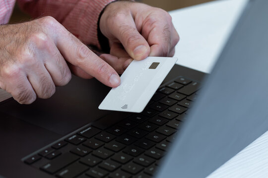 A person is holding a white credit card in front of a laptop and pointing at the card number.