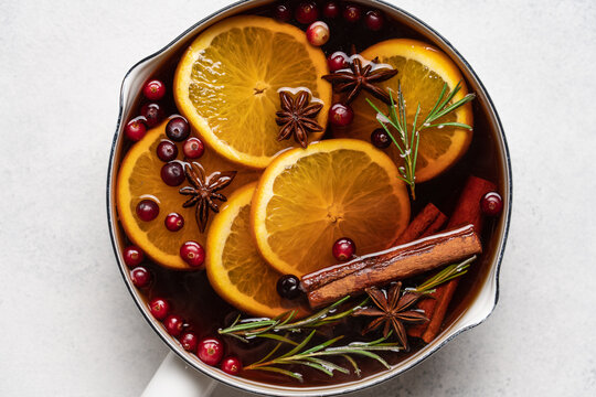 Hot mulled wine with cranberries, orange, rosemary, cinnamon and spices in a pot, Christmas winter drink on a light background with copy space