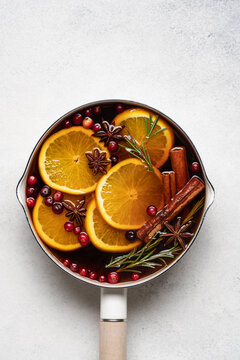Hot mulled wine with cranberries, orange, rosemary, cinnamon and spices in a pot, Christmas winter drink on a light background with copy space