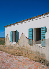 Fischernetz trocknet an der Wand einer typischen Fischerhütte  das "Cason di Pesca" steht auf einer kleiner Insel in der Brackwasserlagune von Comacchio, Holzlamellen kontrastieren zur weißen Wand © michoff
