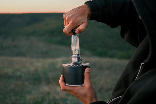Close-up of hands holding a portable camping lamp at sunset, highlighting outdoor lighting equipment for hiking, travel, campsite comfort, and evening adventure.