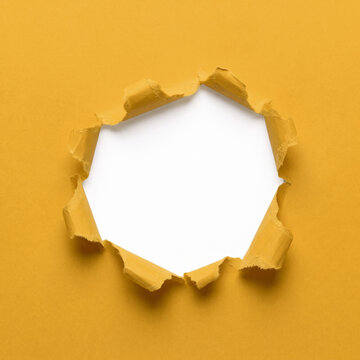 Torn yellow paper hole with ragged ripped edges and black copy space background