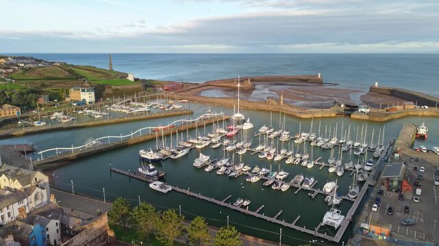 Aerial panoramic views of Whitehaven coastal town and civil parish. Marina and boats demonstration looking to the Irish sea in Sunrise, golden hour. Drone POV exploration of Devon County, England, UK.