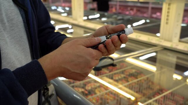Customers hands hold package of sauce on counter background in supermarket. Choosing and buying food at store. Shopping, purchase. Read label
