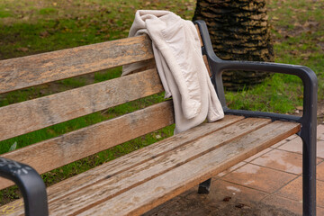 Cream fleece jacket draped over a weathered park bench outdoors.  © Katerina
