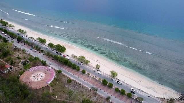 Aerial view white sand beach, turquoise ocean water and park with cars below in Dili, Timor-Leste, Southeast Asia