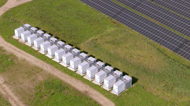 An aerial perspective showcasing a row of industrial battery storage containers integrated into a commercial photovoltaic facility. This setup illustrates modern renewable tech and sustainable resourc