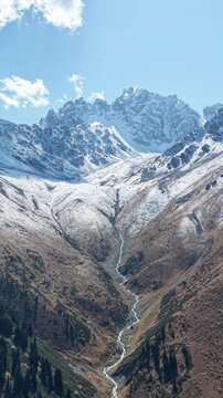 Vertical 9:16 4K drone video pull away and panning across fresh September snow on glaciers, mountain river stream and coniferous forest near Akbulak in Tian Shan mountains, Kazakhstan at morning