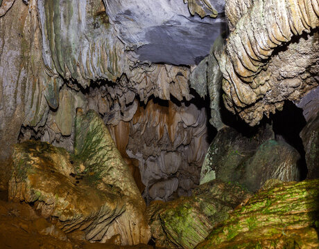 Cave interior showcasing layered stalactites and moss-covered limestone formations near Vang Vieng, Laos.