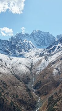 Vertical 9:16 4K drone video pull away and panning across fresh September snow on glaciers, mountain river stream and coniferous forest near Akbulak in Tian Shan mountains, Kazakhstan at morning