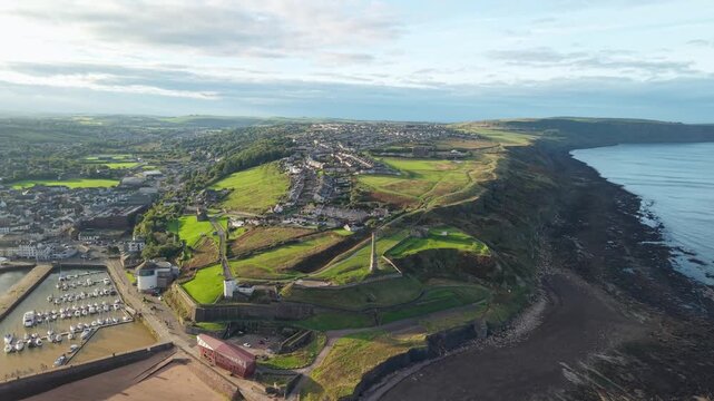 Aerial panoramic views of Whitehaven coastal town and civil parish. Town centre with architecture and main roads with moving vehicles in Sunrise, golden hour. Drone POV exploration of Devon County, UK