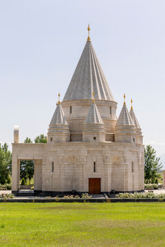 Vertical view of the Quba Mere Diwane Yezidi temple shows its white stone conical towers and golden spires with an entrance door framed against a bright blue sky, Aknalich, Armenia