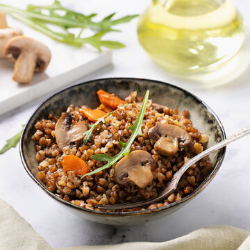 Buckwheat porridge with sauteed champignons and carrots garnished with arugula in ceramic bowl