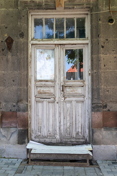 Old weathered wooden double door with peeling paint and glass panels set symmetrically into the stone facade of a historic building along a quiet city sidewalk, Gyumri, Armenia