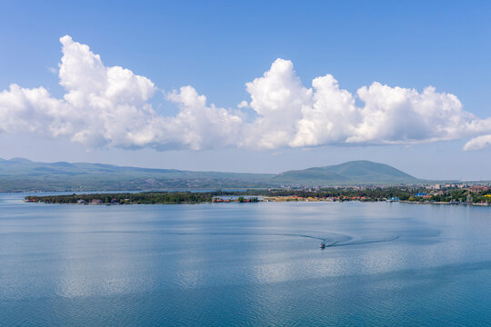 Scenic panoramic view of Lake Sevan with a small wooden boat sailing calmly near the shore beneath a cloudy sky surrounded by distant highland mountains, Sevanavank, Armenia