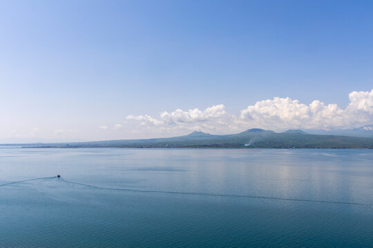Calm tranquil waters of Lake Sevan beneath an overcast cloudy sky with a small boat sailing quietly near the distant shore and highland village waterfront, Sevanavank, Armenia