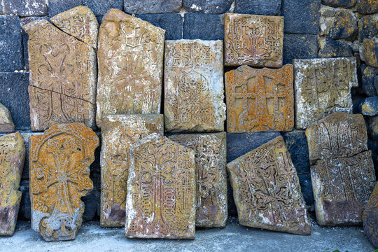Intricately carved khachkar stone crosses with ornamental religious patterns mounted on an ancient weathered wall at Sevanavank Monastery covered with lichen, Sevanavank, Armenia