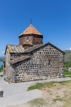 Surp Astvatsatsin stone church with its bell tower and cross standing on the scenic shore of Lake Sevan beneath distant mountains under a clear blue sky, Sevanavank, Armenia