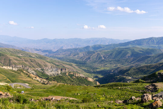 Panoramic view of a lush green mountain valley with a winding road curving past hills and a canyon while a camper van travels the route, Selim, Armenia