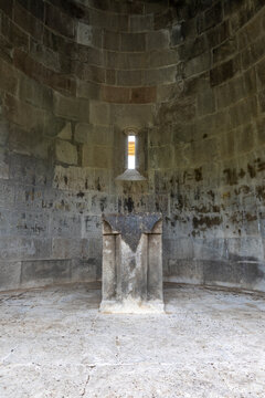 Stone altar stands inside the curved apse of an ancient orthodox church beneath a narrow window where soft light reveals old wall inscriptions, Eghegis, Armenia