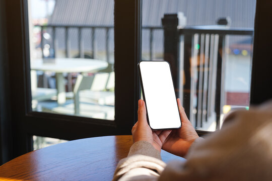 Mockup image of a woman holding mobile phone with blank desktop screen in cafe