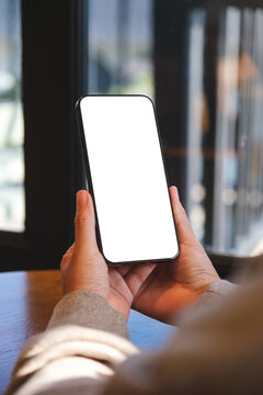 Vertical mockup image of a woman holding and using mobile phone with blank desktop white screen in cafe