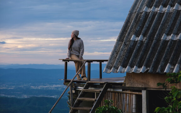 A woman sitting on wooden balcony and looking at mountain views on cloudy morning